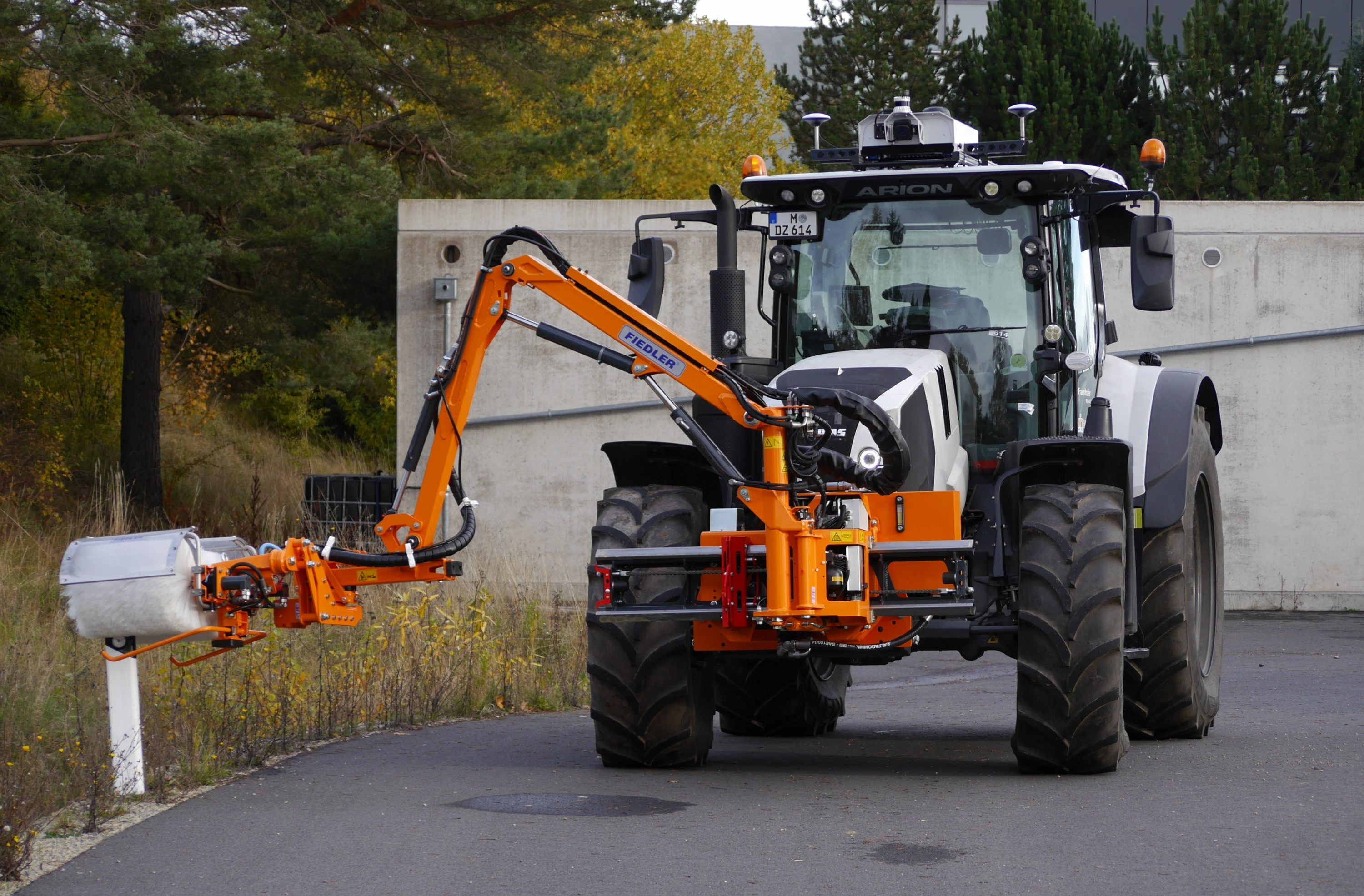 Im „Reallabor für autonome Arbeitsmaschinen“ am Fraunhofer IOSB-AST in Ilmenau reinigt der autonome Traktor ARION mithilfe eines Anbaugeräts einen Leitpfosten. 